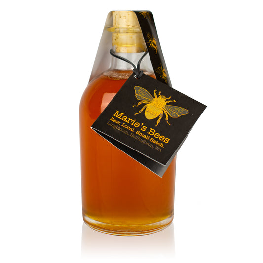 A glass bottle filled with amber-colored honey, sealed with a cork, and labeled with a black and yellow bee-themed tag.
