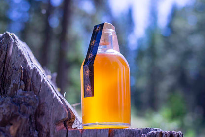 A glass bottle filled with amber-colored honey, sealed with a cork, and labeled with a black and yellow bee-themed tag.