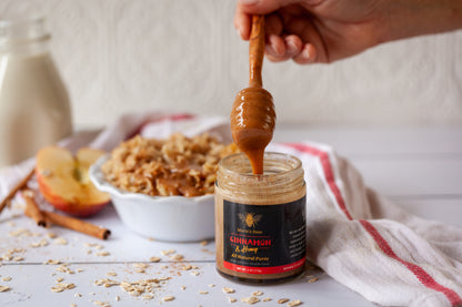A jar of cinnamon creamed honey with a honey dipper resting on top, with a spread of oatmeal and fruits in the background.
