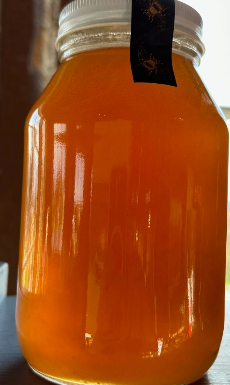 A glass jar filled with raw honey, with a white lid and a label that reads 'Marie's Bees Raw Honey'.