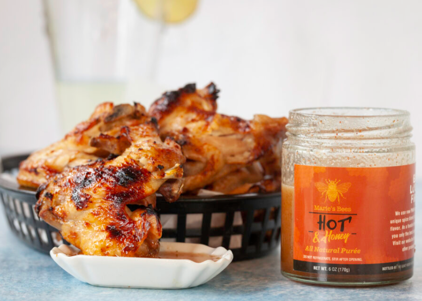 A jar of Hot Creamed Honey next to a basket of grilled chicken wings.