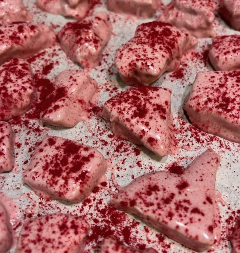A close-up of raspberry white chocolate honeycomb candy with a glossy, wet appearance, sprinkled with red raspberry powder.